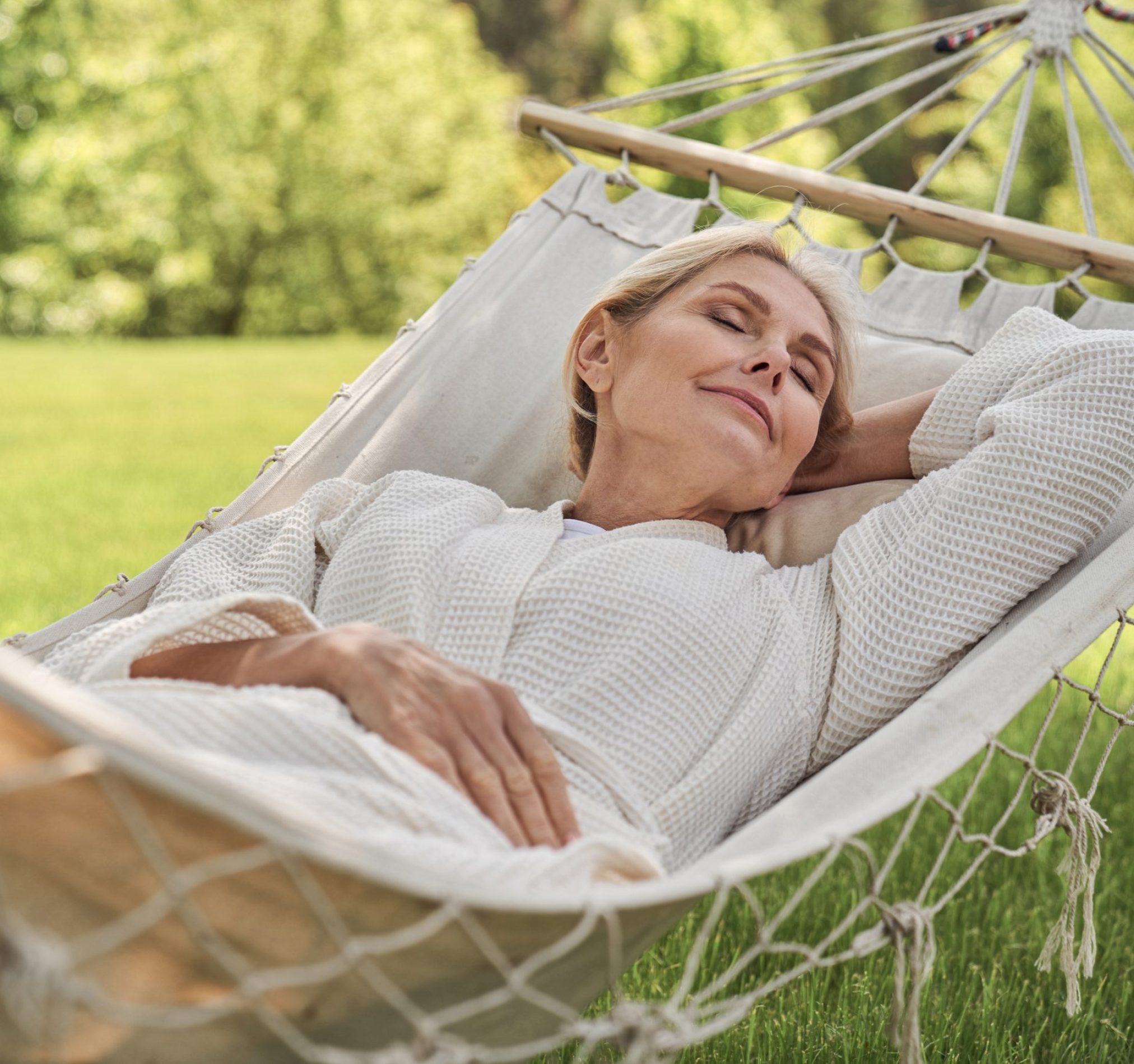 Smiling beautiful woman is having rest in green yard in open air on sunny warm day